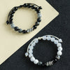 Two beaded bracelets with black and white stones and a silver snake charm on a two-tone background