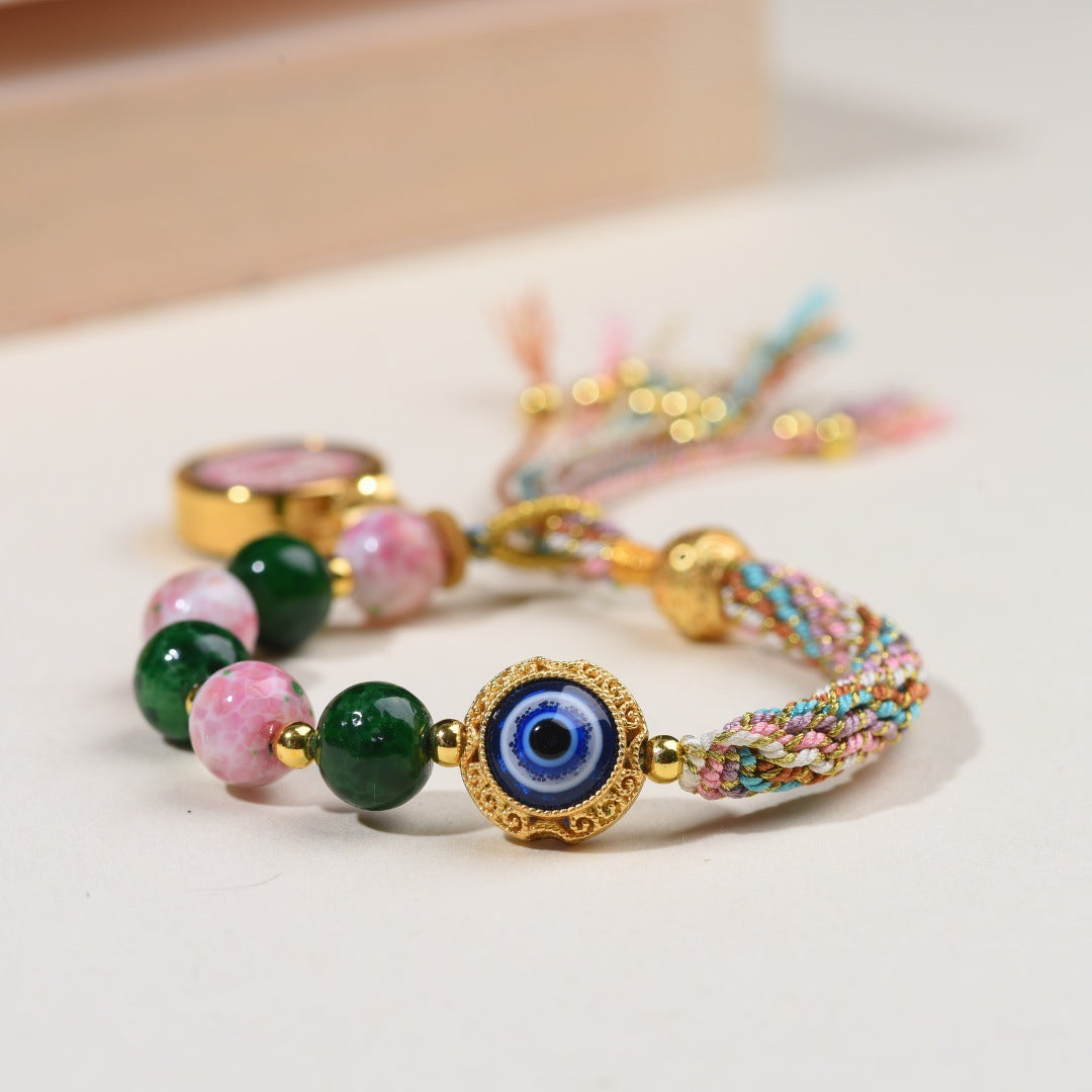 Close up of a multicolor woven bracelet with a blue evil eye charm and green beads