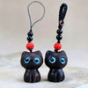 Two wooden cat charms, one dark ebony and one reddish brown, sitting side by side.