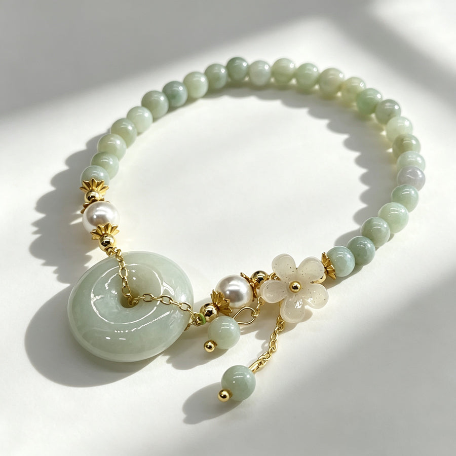 Pale green jade bead bracelet with a large round peace buckle charm and a small white flower pendant