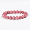 Close up of a pink rhodochrosite beaded bracelet on a white surface