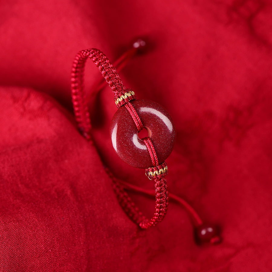 Close-up view of a red braided bracelet with a central red peace buckle charm