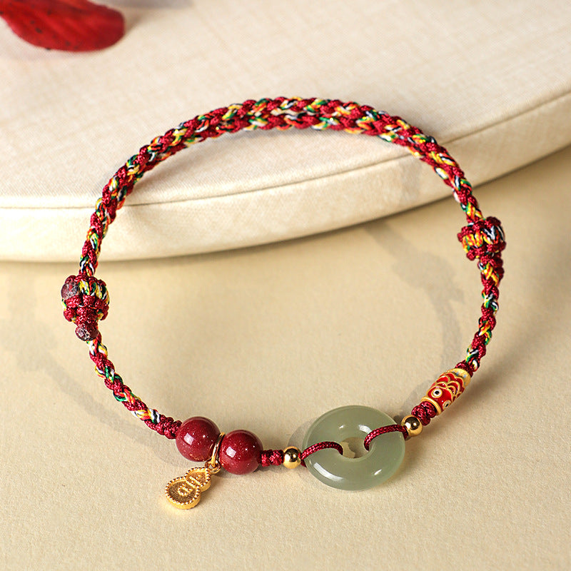Close up of a braided bracelet with a jade donut bead and gold charm