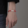 Close-up of a man wearing a red braided bracelet with a silver bar charm on his wrist