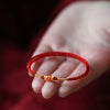 Close up of a red braided bracelet with a gold fish charm held in a hand