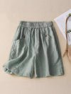 Green cotton linen women's shorts with pockets laid flat on a beige background