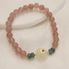 Close-up of a pink beaded bracelet with a white jade center piece on a white surface