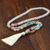 Long natural jade beaded necklace with multicolored stones and a cream tassel on wood