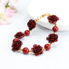 Red cinnabar bracelet with carved rose charms and gold-tone chain clasp on a white surface