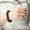 A wrist wearing a dark wooden bracelet with square carved beads