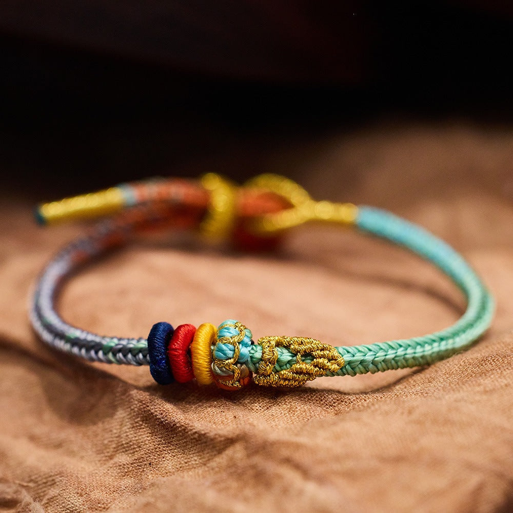 Close-up of a colorful woven cord bracelet with a gold-tone knot on a wooden surface