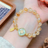 Close up of a yellow citrine beaded bracelet with a green lotus charm resting on a wooden tray