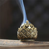 A brass-colored lotus-shaped incense burner with smoke rising from the top.