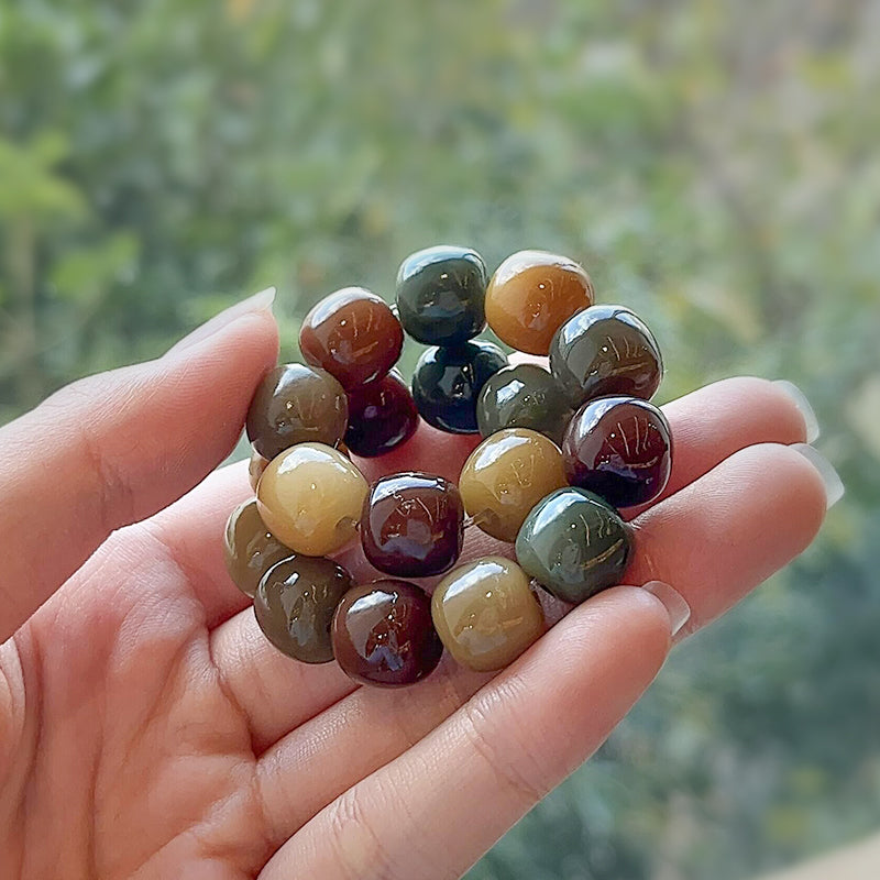 Hand holding a multi-colored bodhi seed bracelet with smooth, rounded beads