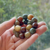 Hand holding a multi-colored bodhi seed bracelet with smooth, rounded beads