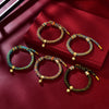 Five colorful handwoven cord bracelets with gold-tone bells arranged on a red background