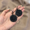 Two round black shungite pendants held in a hand, one with a tree carving and one with a geometric pattern