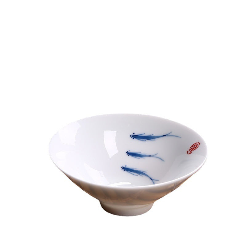 White porcelain teacup with blue hand painted koi fish design on a bamboo mat