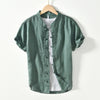 Green linen men's short sleeve shirt with stand collar and frog buttons hanging on a wooden hanger