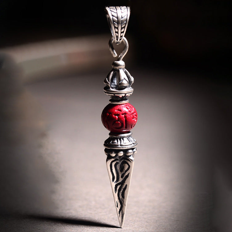 Close up of silver tone vajra pendant with red bead on dark wood