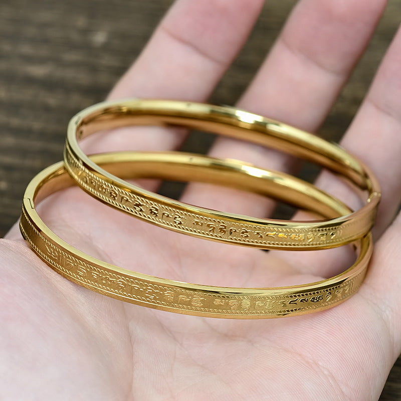 Gold tone and silver titanium steel bangles with engraved mantras held in hand