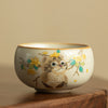 Hand holding a ceramic teacup with a painted cat and yellow flowers design