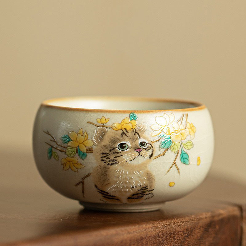 Hand holding a ceramic teacup with a painted cat and yellow flowers design