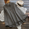 Black and white plaid women's long sleeve shirt with ruffled hem on wooden background