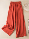 Flat lay of orange wide leg linen pants with a woven bag