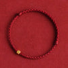 Close up of a red braided bracelet with a single small gold square bead