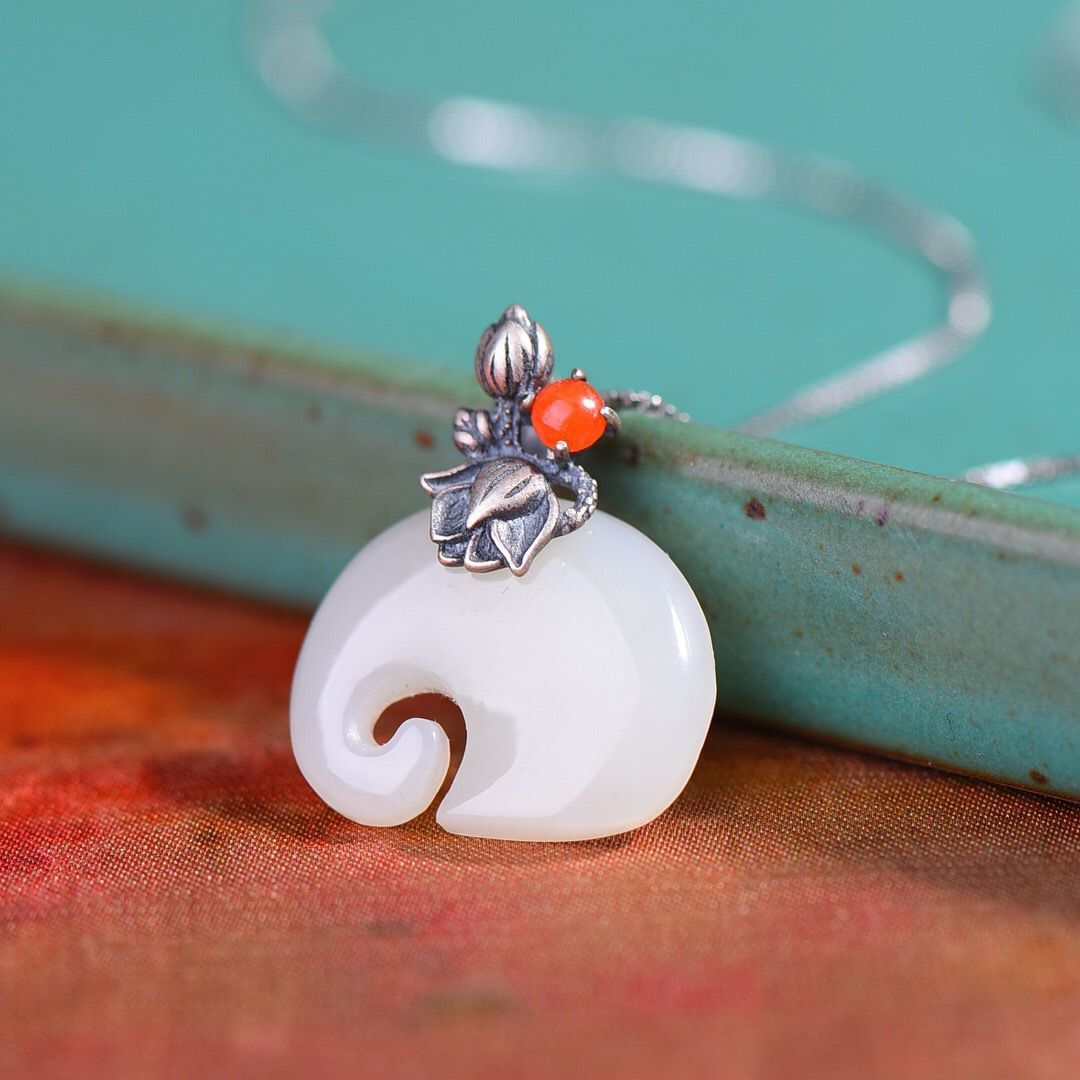 Close up of a white elephant shaped pendant with a silver lotus charm on a chain