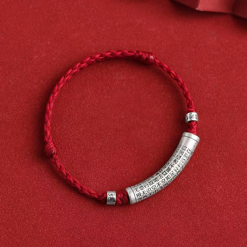 Close up of a red braided bracelet with a silver curved tube engraved with text