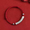 Close up of a red braided bracelet with a silver curved tube engraved with text