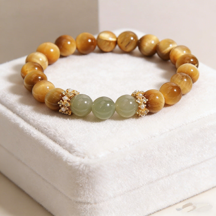 Round golden tiger eye beads with green jade accents on a white display cushion
