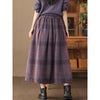 Woman wearing a long purple and brown plaid wool skirt with hands in pockets
