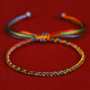 Close-up view of a hand-braided multicolored cord bracelet with a sliding knot on a red background