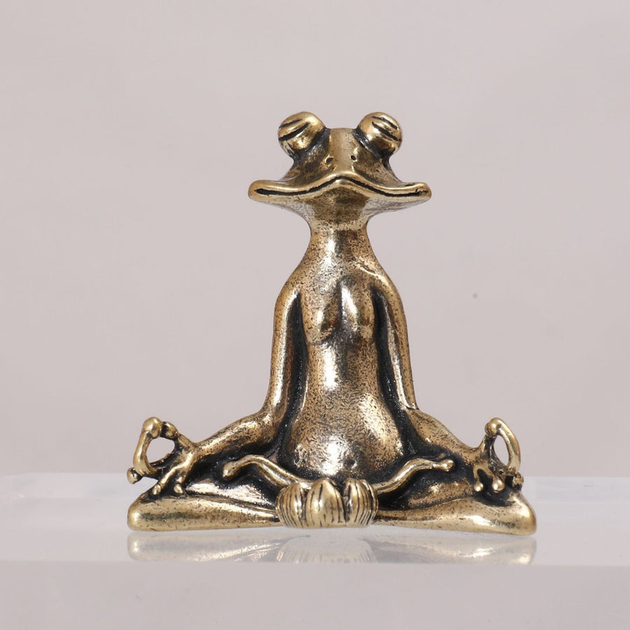 Close up of a small brass frog sitting in a yoga pose on a wooden table
