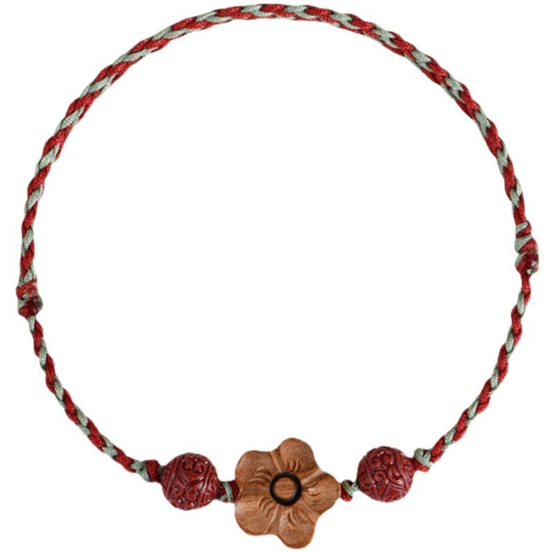 Close up of a braided red string bracelet with a wooden flower charm and red beads on a tan background