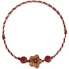 Close up of a braided red string bracelet with a wooden flower charm and red beads on a tan background