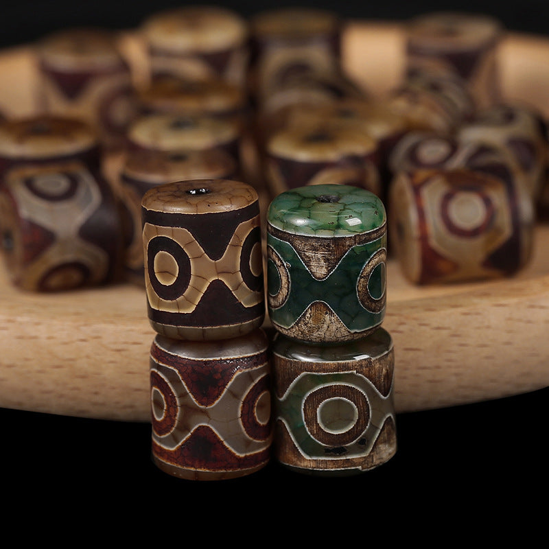 Close-up of stacked green and brown carved agate Dzi beads on a wooden surface.