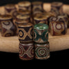 Close-up of stacked green and brown carved agate Dzi beads on a wooden surface.