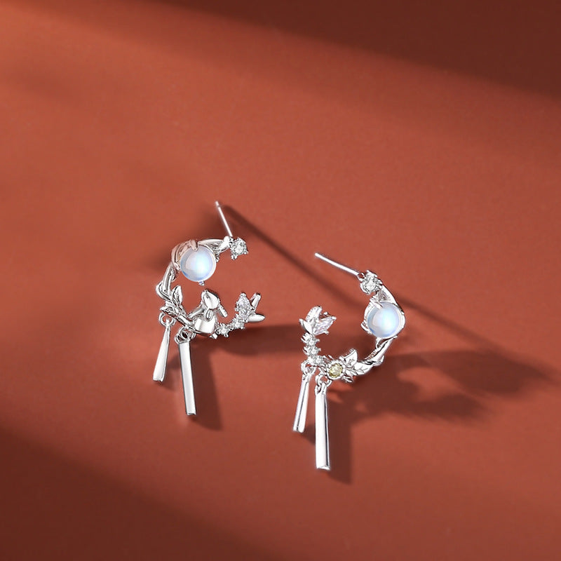 Close-up of silver rabbit hoop earrings with dangling bars and moonstone accents