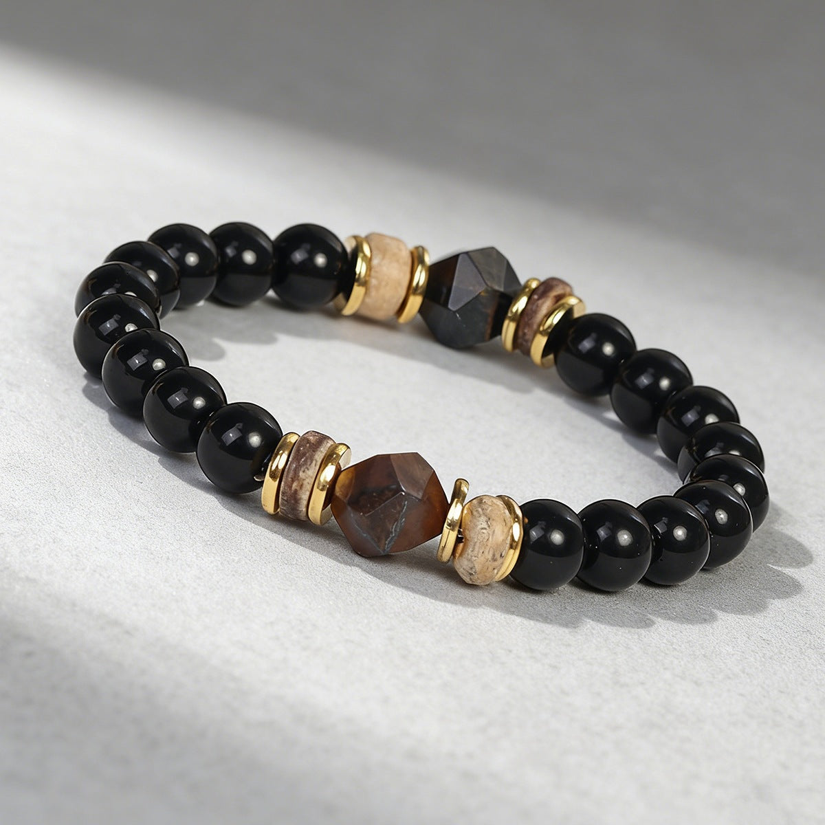 Close-up of a beaded bracelet with black and brown faceted stones on a light background