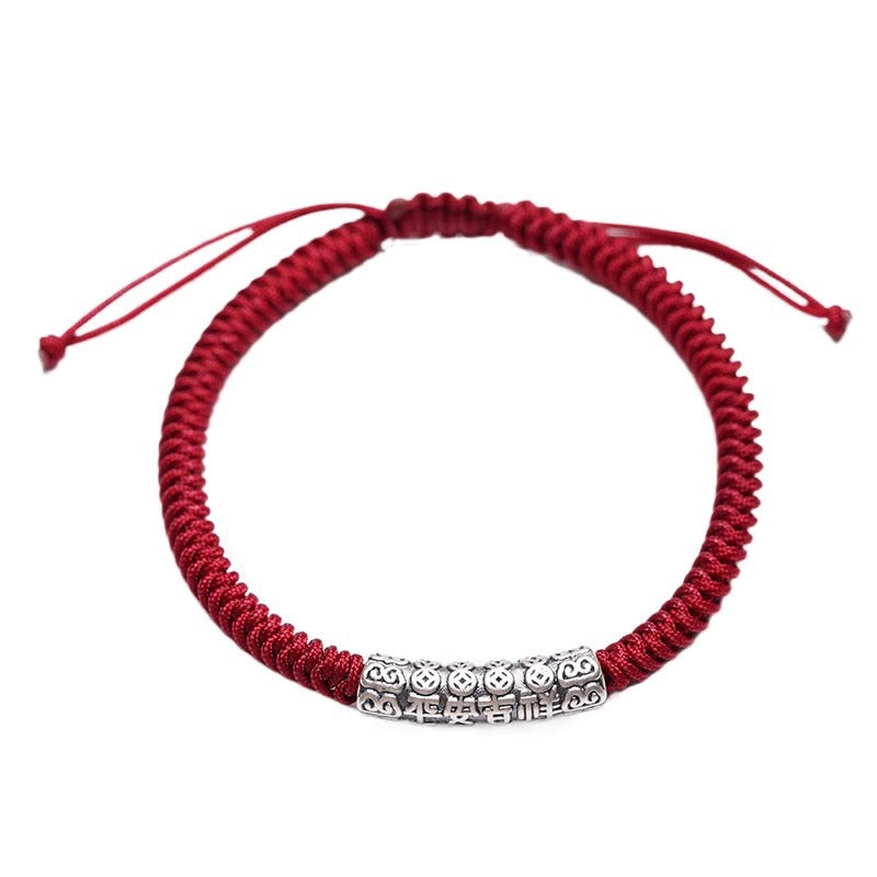 Close up of a red woven cord bracelet with a silver tone cylindrical bead engraved with Tibetan script.