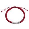 Close up of a red woven cord bracelet with a silver tone cylindrical bead engraved with Tibetan script.