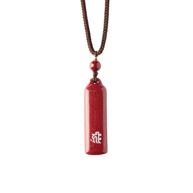 Red cylindrical cinnabar pendant with white Sanskrit script on a brown cord