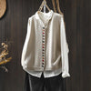 Beige cotton knit vest with colorful buttons hanging on a wooden branch against a dark wall.
