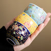 Three enamel painted ceramic tea cups with lotus patterns held in a hand