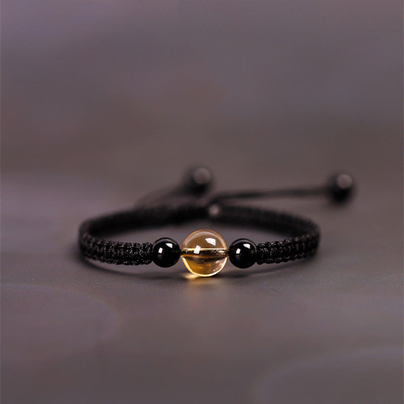 Close up of a black woven cord bracelet with a yellow citrine bead center