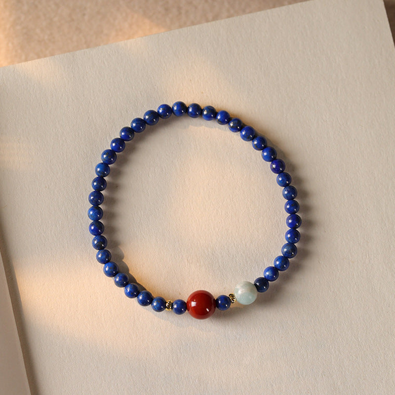 Close up view of a thin blue lapis lazuli beaded bracelet with one red bead